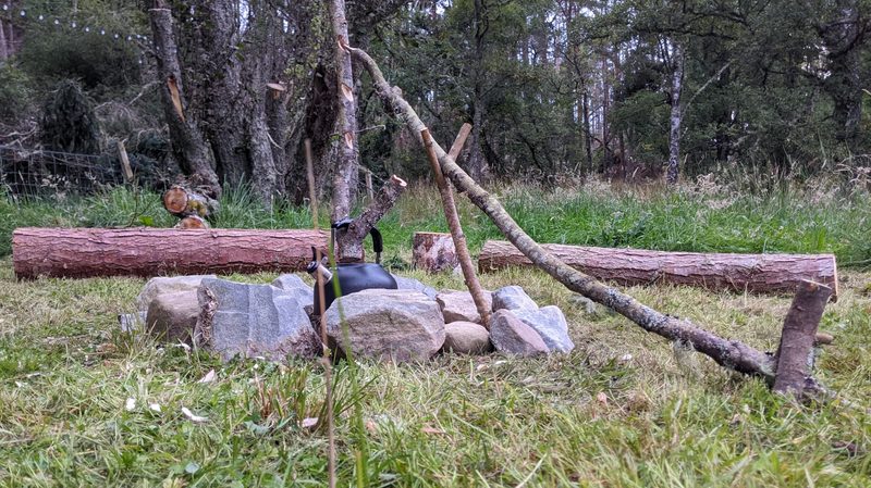 A campfire pot hanger with a kettle hanging over a circle of stones