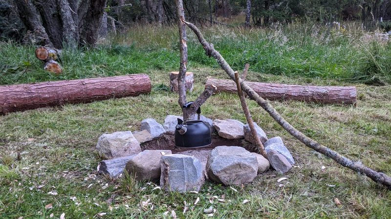 A campfire pot hanger holds a kettle over a stone circle