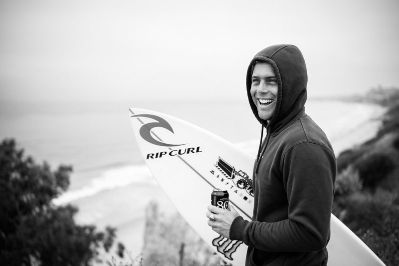 Conner Coffin with a surf board and beer in hand.