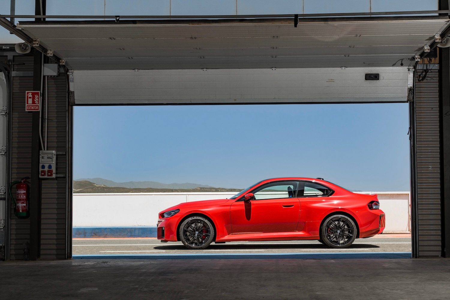 2023 BMW M2 side from inside a garage with blue skies in the back.