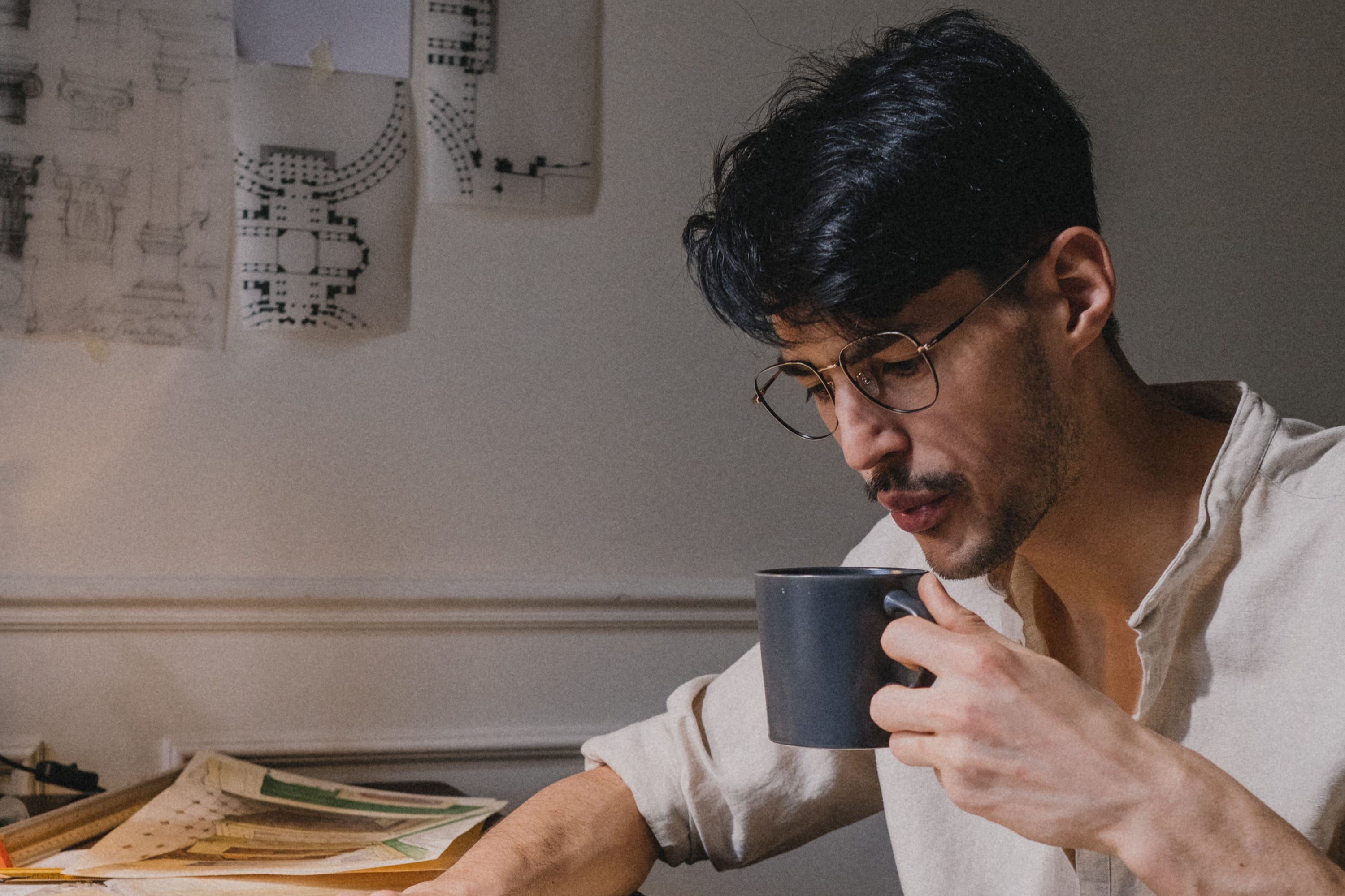 man drinking coffee surrounded by papers