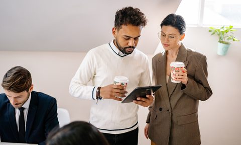 A man in a crewneck sweater speaking with a woman in a blazer