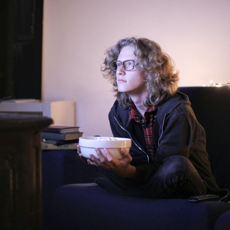 A person on their couch watching TV with popcorn