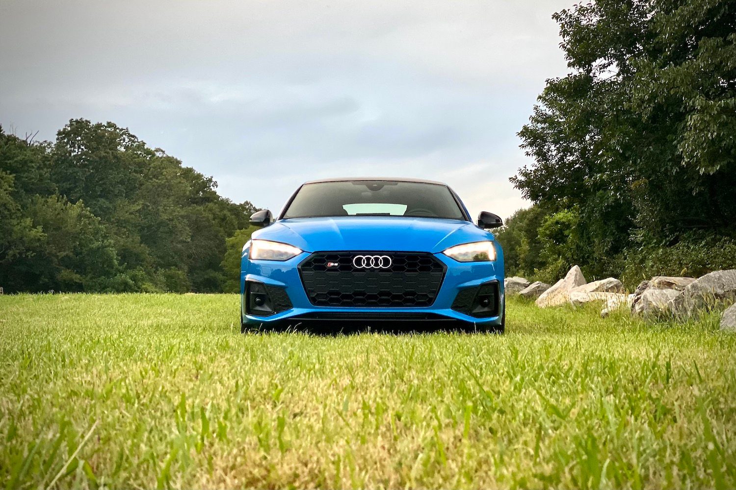 Close up of front end of 2023 Audi S5 Sportback in a grassy field during sunset.