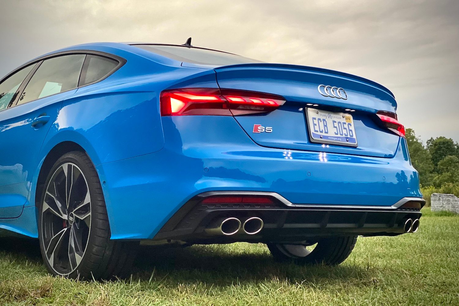 Rear end close up of 2023 Audi S5 Sportback during sunset in a grassy field.