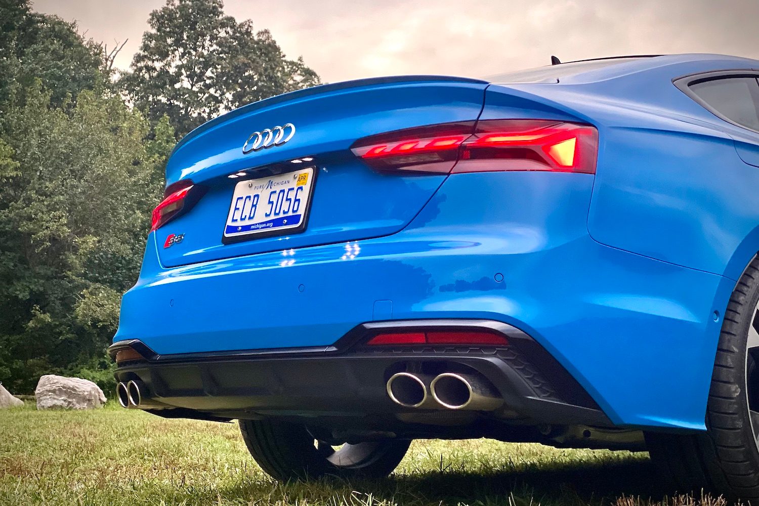 Close up of rear end of 2023 Audi S5 Sportback from below with trees in the back.