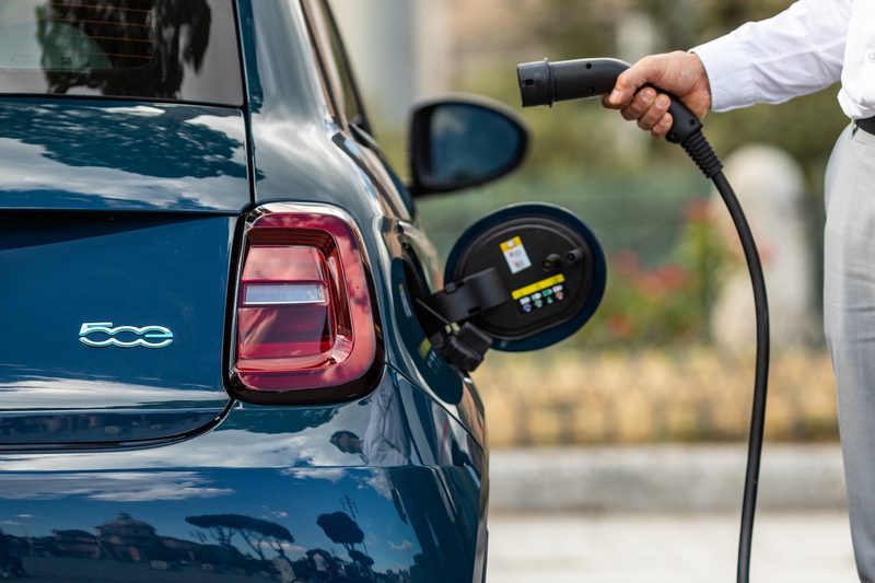 Man plugging an electric charger into the 2024 Fiat 500e in a city.
