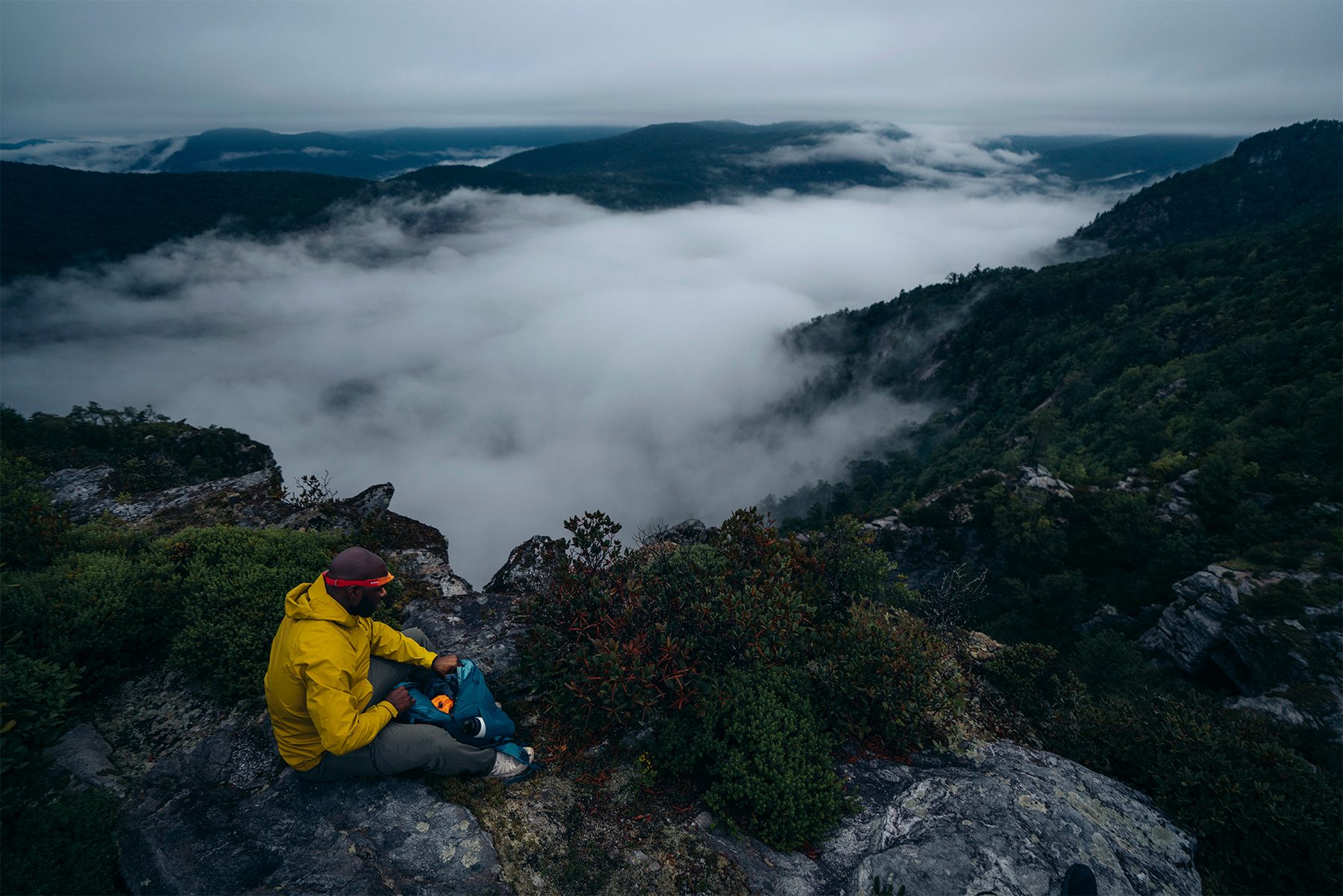 A man sits overlooking a cloud inversion while wearing the BioLite HeadLamp 425