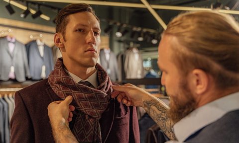A man tying scarf for another man in a store