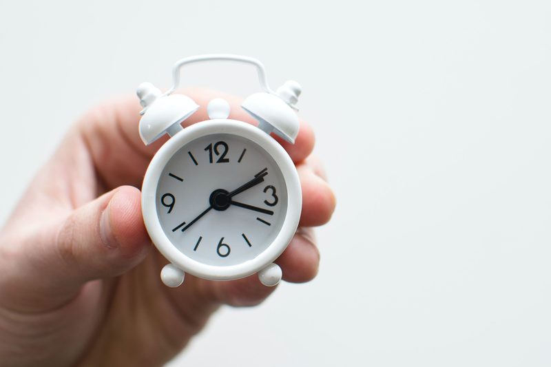 person holding small alarm clock in hand