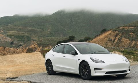 White Tesla in front of a lush green mountain range