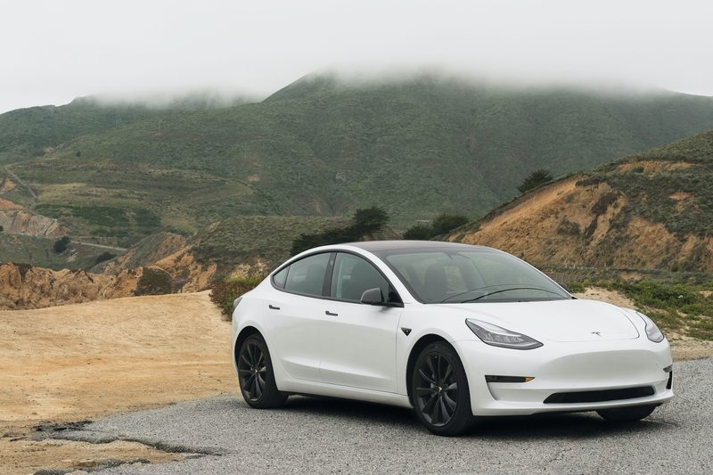 White Tesla in front of a lush green mountain range