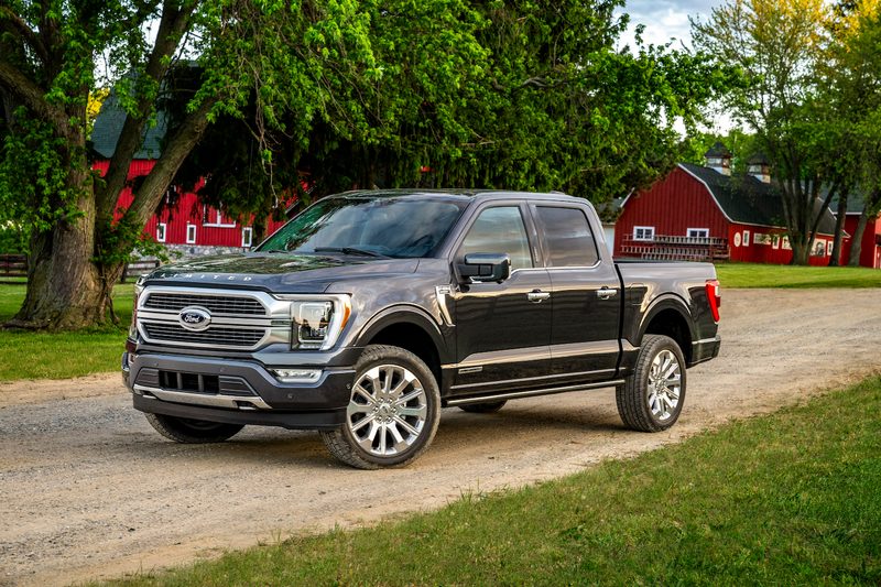 Front end angle of 2021 Ford F-150 parked on a dirt trail in front of a red barn and trees.