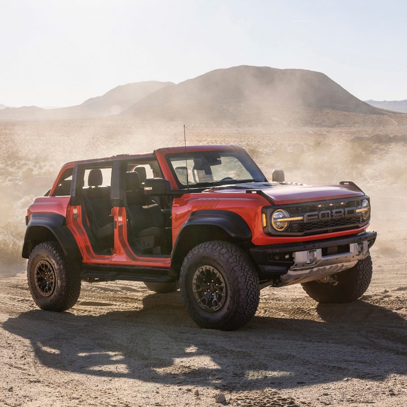 2022 Ford Bronco Raptor off-roading through sand dunes with the doors and roof off the SUV with a dust cloud in the back.