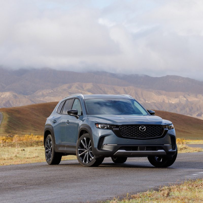 2022 Mazda CX-50 front end angle from passenger's side with rolling hills in the background with dark clouds.