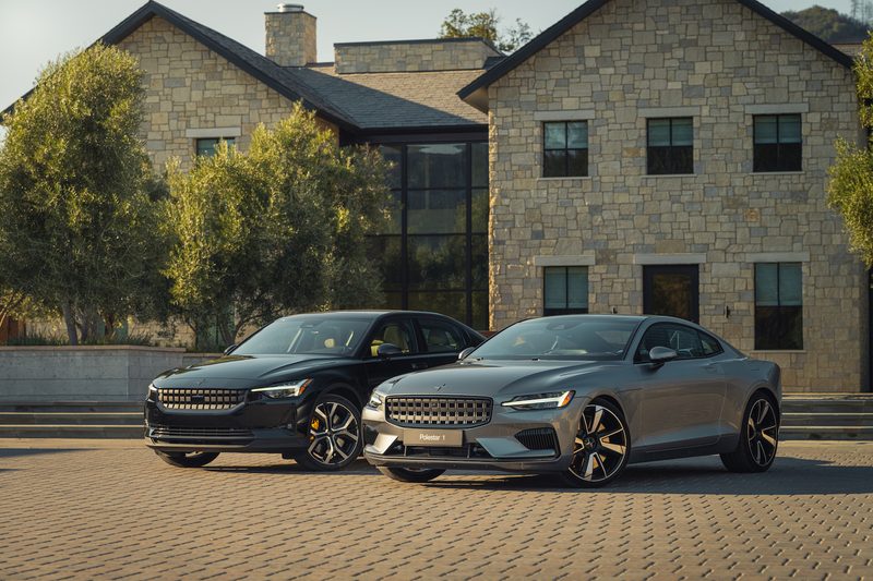 Front end angles of 2022 Polestar 1 and Polestar 2 electric cars in front of a brick hotel on a brick path.