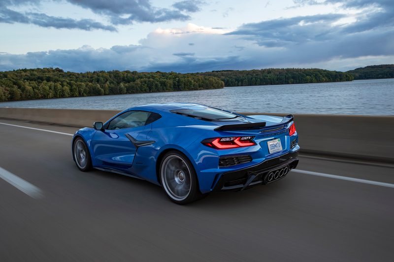 2023 Chevrolet Corvette Z06 rear end angle from driver's side driving on the road in front of a body of water with clouds in the back.