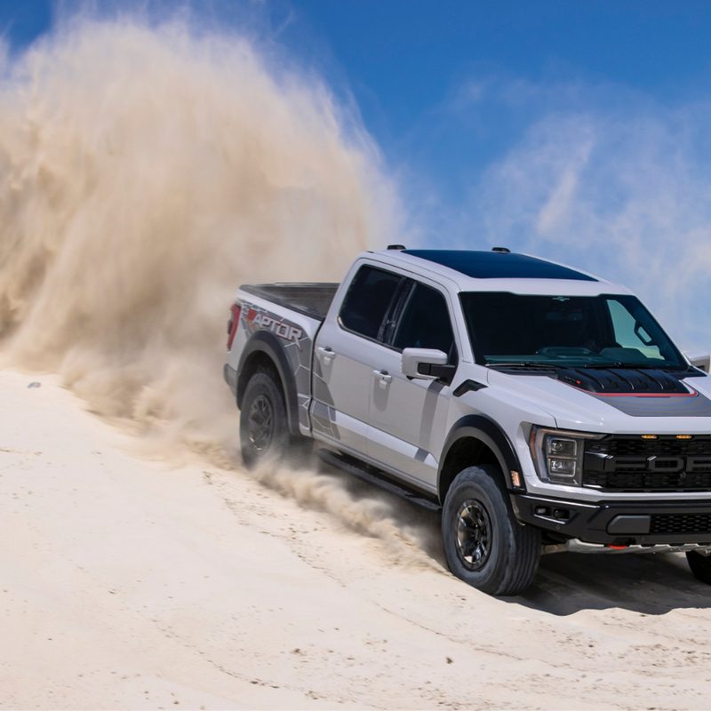 2023 F-150 Raptor R front end from passenger's side driving own a sand dune with blue skies in the back.