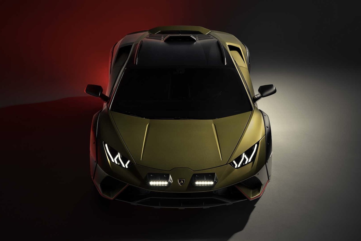 Close up of front end of 2023 Lamborghini Huracan in a studio with red, white, and black lighting with headlights on.