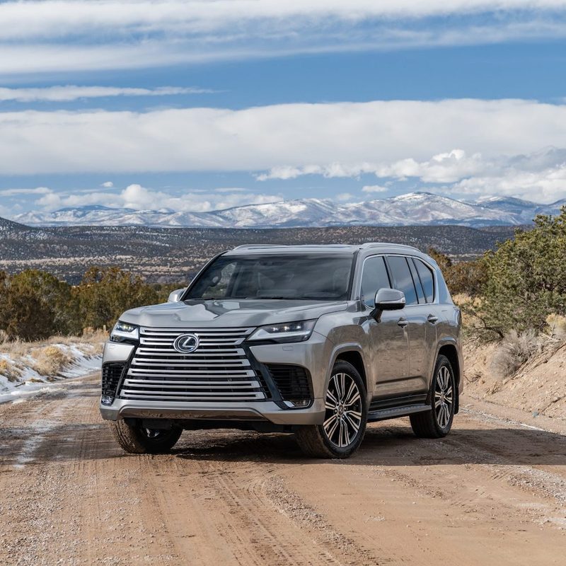 2023 Lexus LX600 front end angle from driver's side on a dirt trail in front of mountains and snow on the ground.