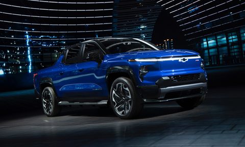 2024 Chevrolet Silverado EV RST pickup truck front end angle from passenger's side parked under a light with large window and buildings in the back.