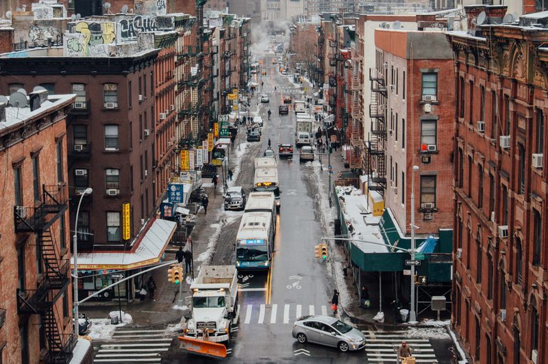 East coast city in winter with snow on the ground and on top of apartment buildings with cars on the road.
