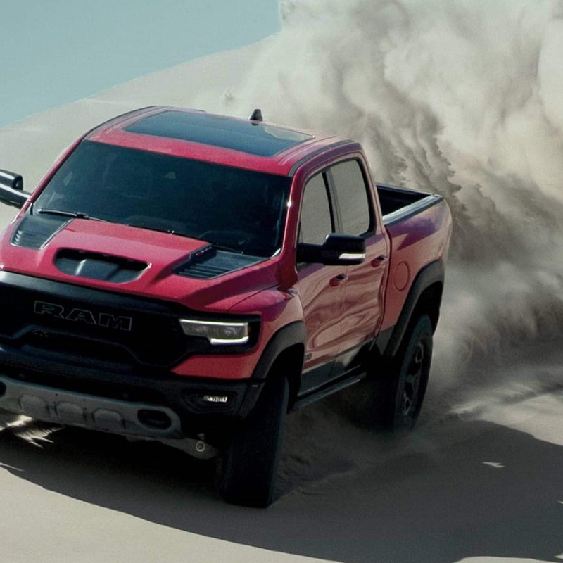 Front end of 2022 Ram 1500 TRX power sliding on a sand dune in the desert with blue skies in the back.