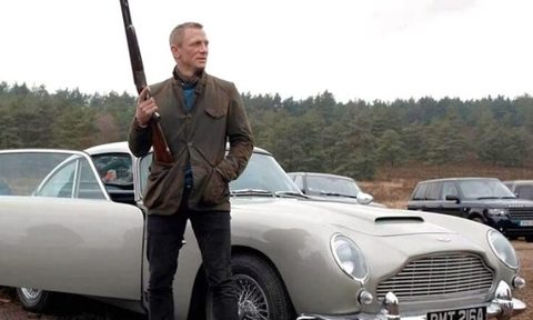 James Bond holding a shotgun and standing next to an Aston Martin