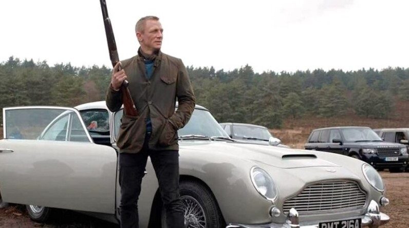 James Bond holding a shotgun and standing next to an Aston Martin