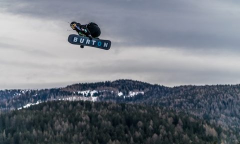 A snowboarder rides high over a jump on a Burton Snowboard.