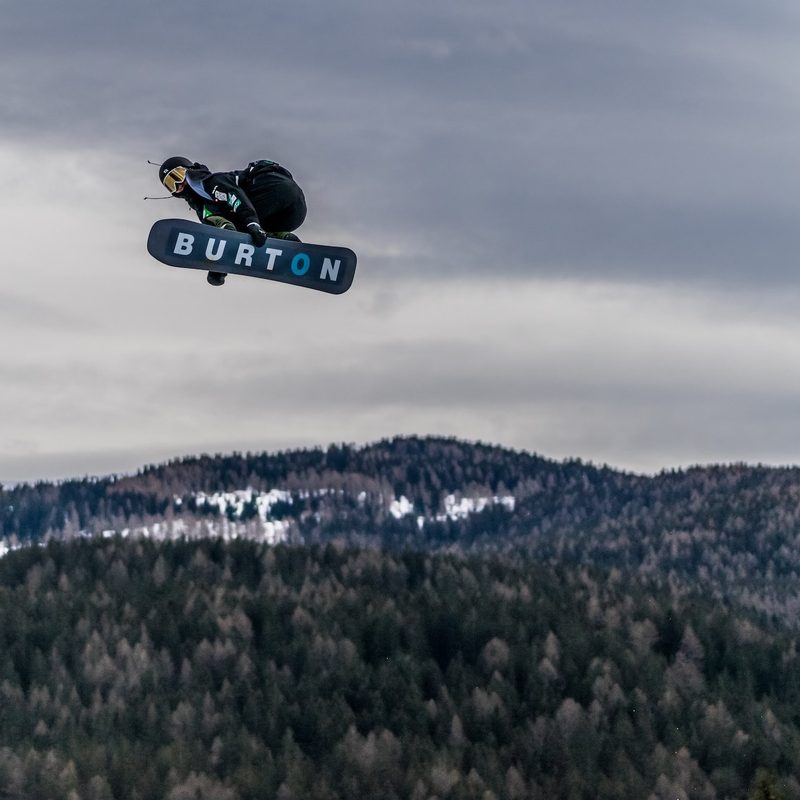 A snowboarder rides high over a jump on a Burton Snowboard.
