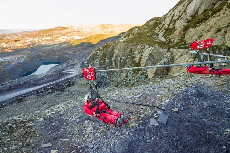 Two people in red jumpsuits ziplining in Wales.