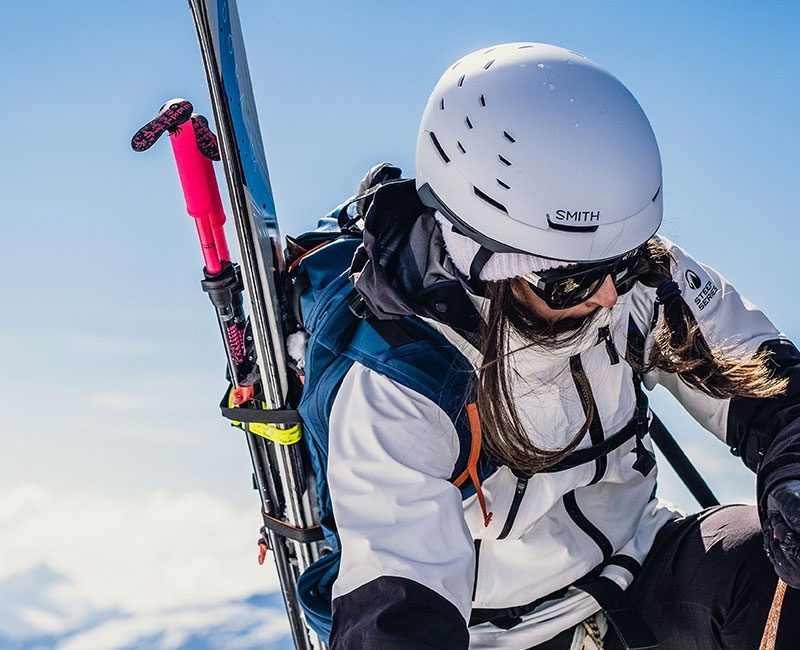 Woman with skis climbing mountain wearing Smith Summit Helmet.