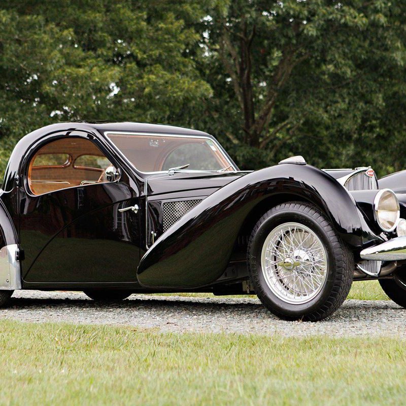 1937 BUGATTI TYPE 57SC ATALANTE side profile from passenger side parked in a field with green trees in the back.