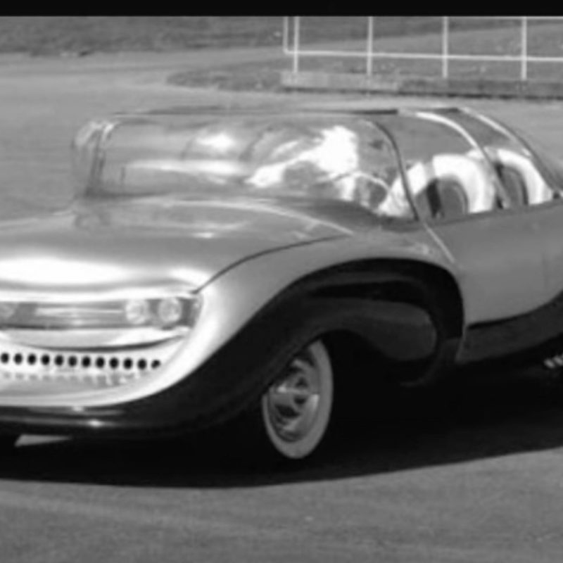 Front end angle of 1957 Aurora Safety Car from driver's side parked in a dirt parking lot.