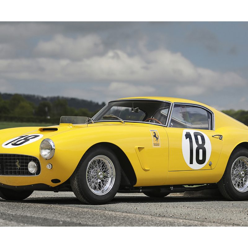 1960 Ferrari 250 GT SWB Berlinetta Competizione front end angle from driver's side parked in font of green hills and clouds.