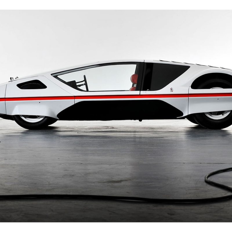 Side profile of 1970 Ferrari Modulo parked in front of a white wall on top of a gray floor.
