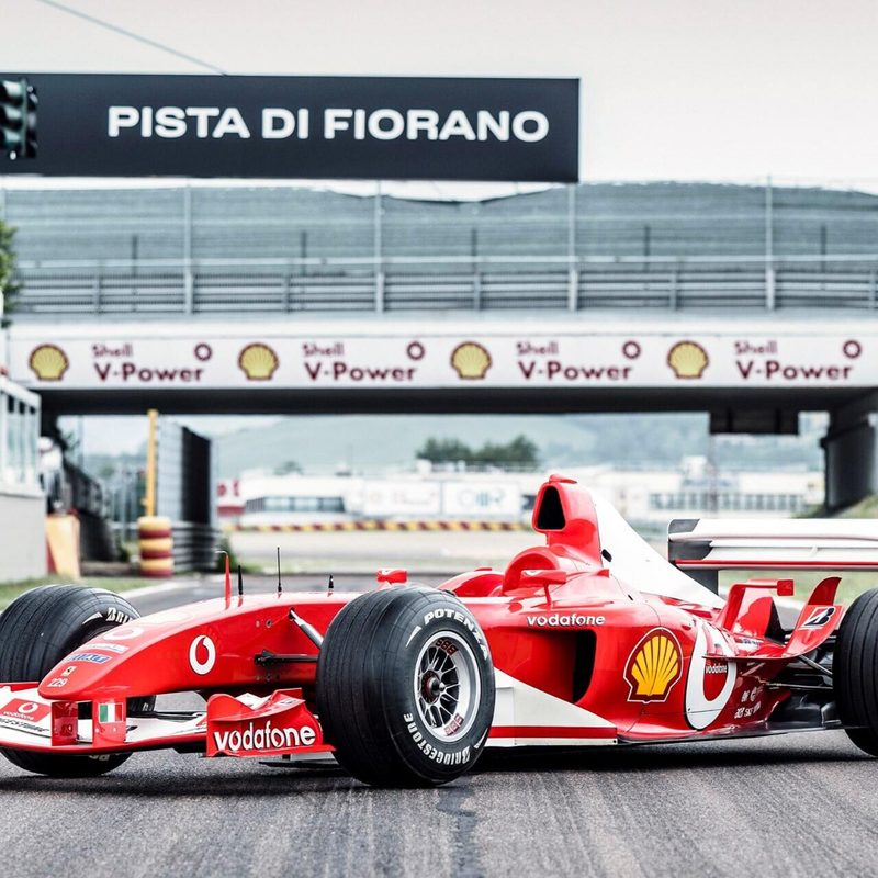 2003 Ferrari F2003 GA race car front end angle parked in the middle of a race track.