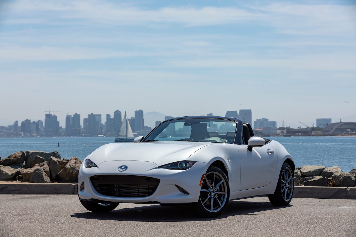 2019 Mazda MX-5 Miata front end angle from driver's side with top down parked in front of a city skyline.