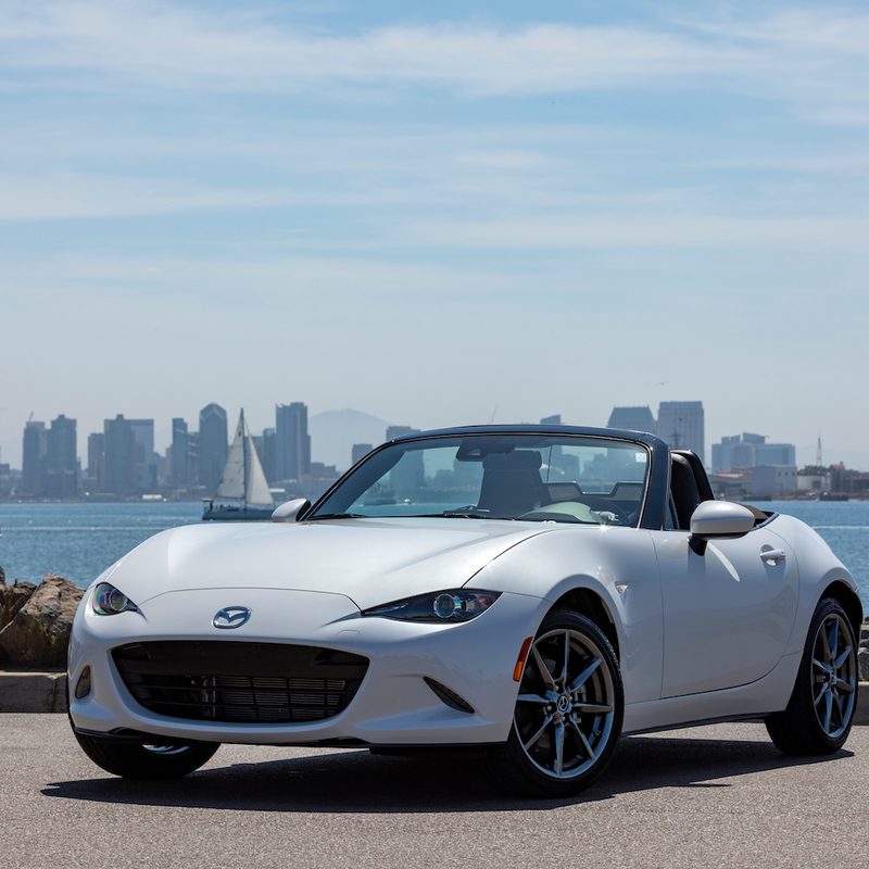 2019 Mazda MX-5 Miata front end angle from driver's side with top down parked in front of a city skyline.
