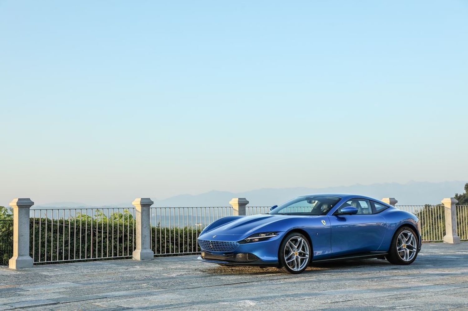 2021 Ferrari Roma front end angle from driver's side with a metal fence and blue skies in the back.