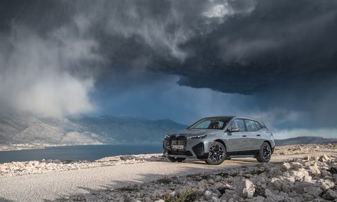 2022 BMW iX xDrive50 front end angle in front of dark storm clouds on a dirt trail.