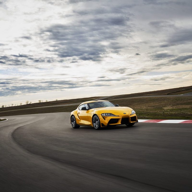 2022 Toyota GR Supra 2.0 front end driving on a race track with clouds in the back ground.