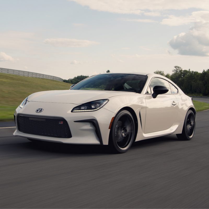2022 Toyota GR86 Premium front end angle driving on a race track with green trees in the back.