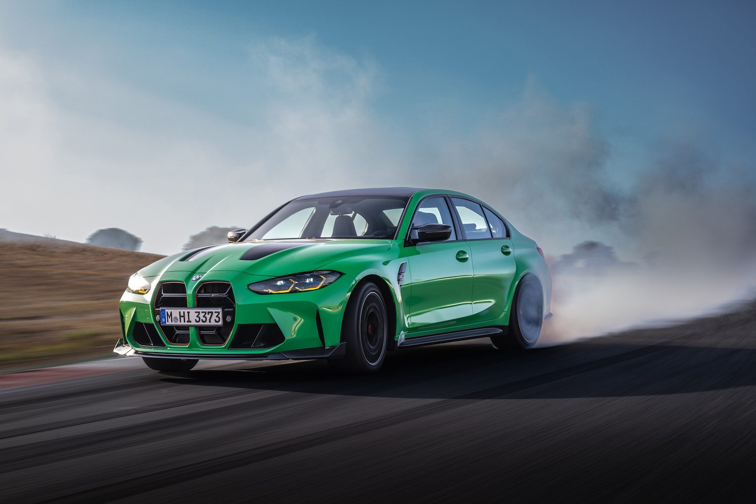 2024 BMW M3 CS doing a smoky burnout on a road with dirt in the back.