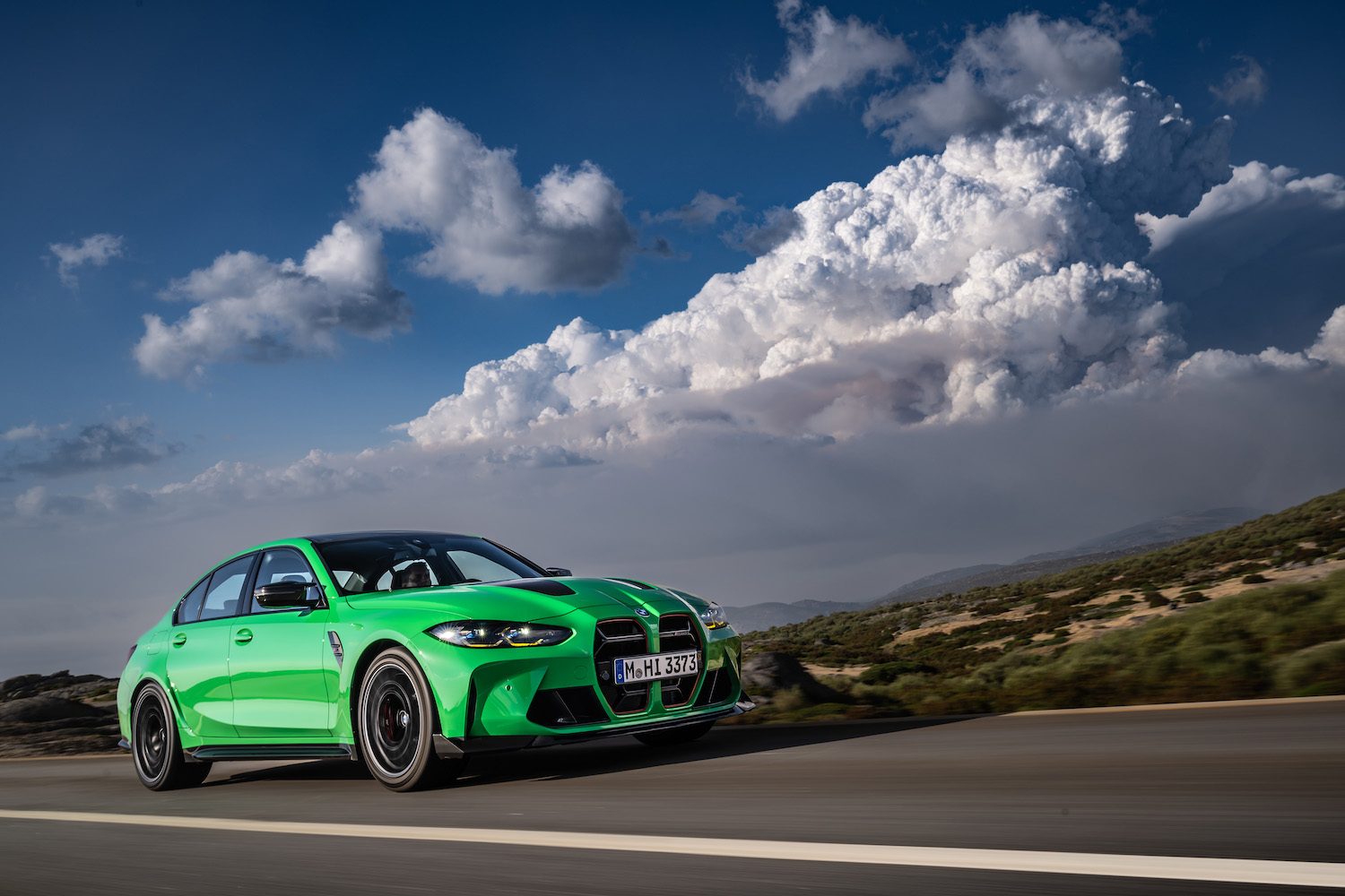 Front end angle of 2024 BMW M3 CS from passenger side driving down the road with clouds in the back.