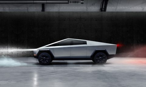 Tesla Cybertruck parked indoors in front of a black wall with headlights and taillights on.