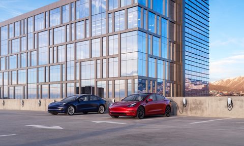 Tesla Model 3s charging outside of a work building in a parking lot.