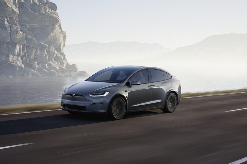 Tesla Model X front end angle driving down the road with mountain cliffs in the back.