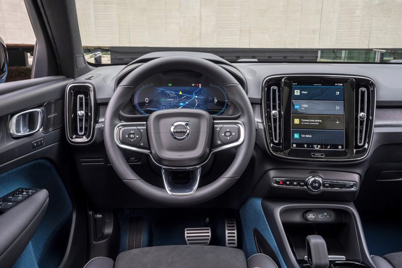 Close up of steering wheel, dashboard, and touchscreen in the Volvo C40 Recharge with a building in the back.
